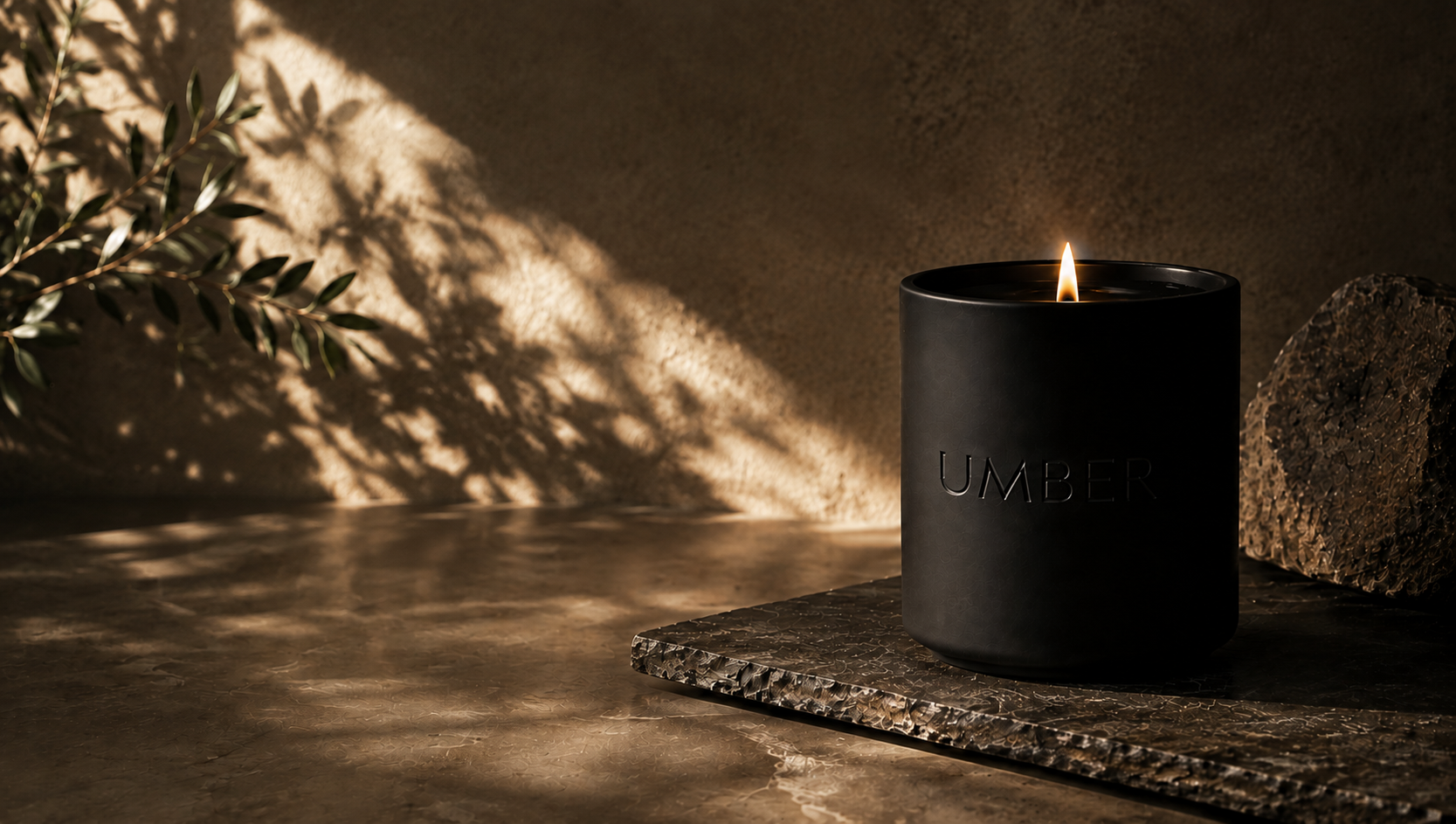 An UMBER candle burning in warm, dappled light on a stone surface
